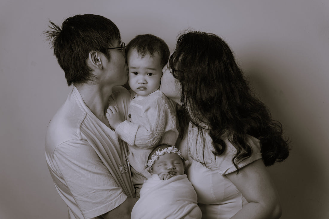 a family photo of a son and daughter, both hold by each parents, parent kissing the elder son, who look confused. 