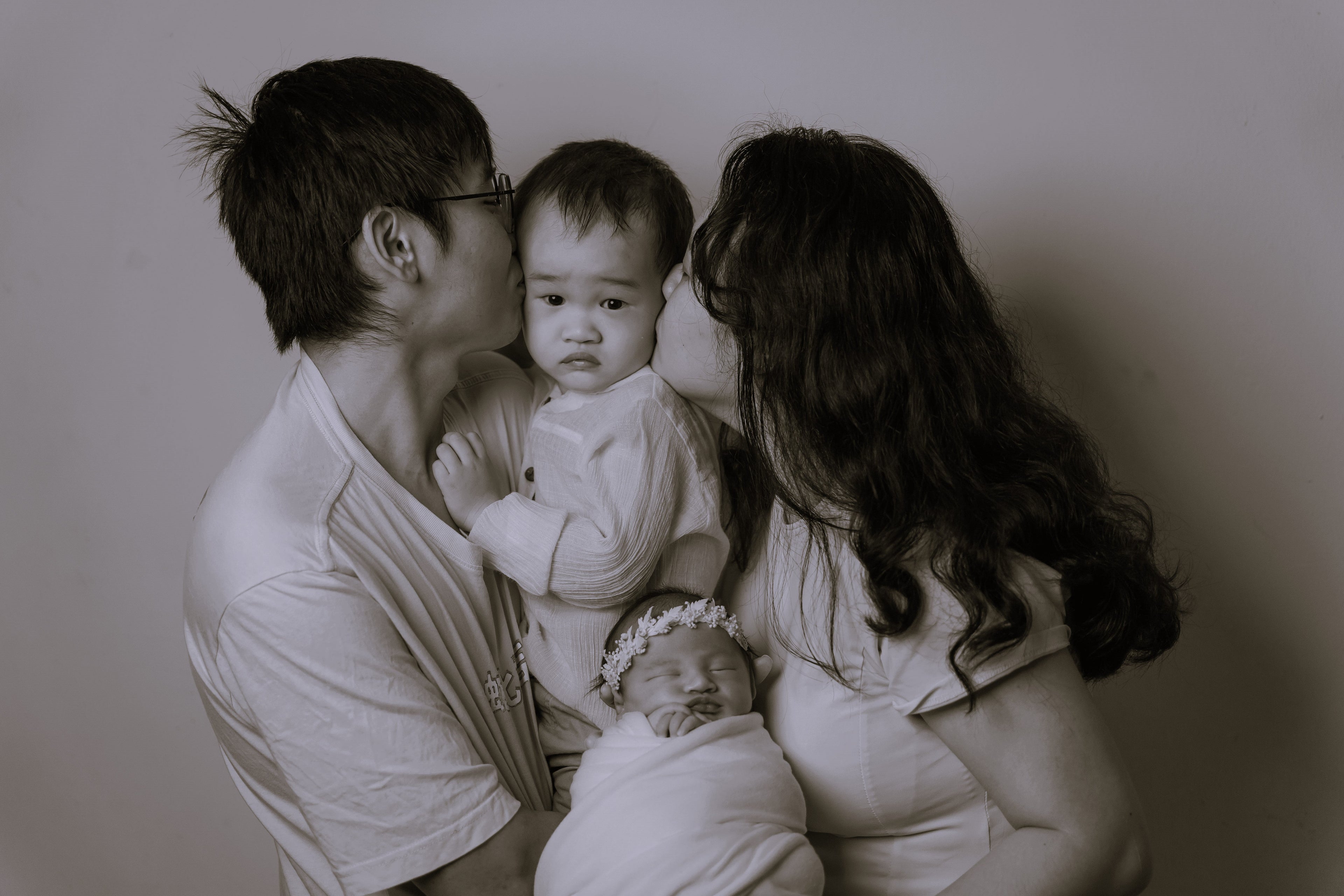 a family photo of a son and daughter, both hold by each parents, parent kissing the elder son, who look confused. 