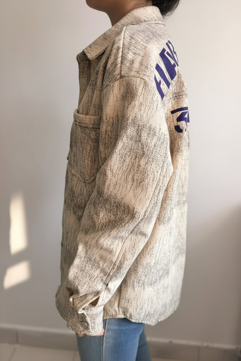 Person wearing a beige jacket with text on the sleeve against a plain background