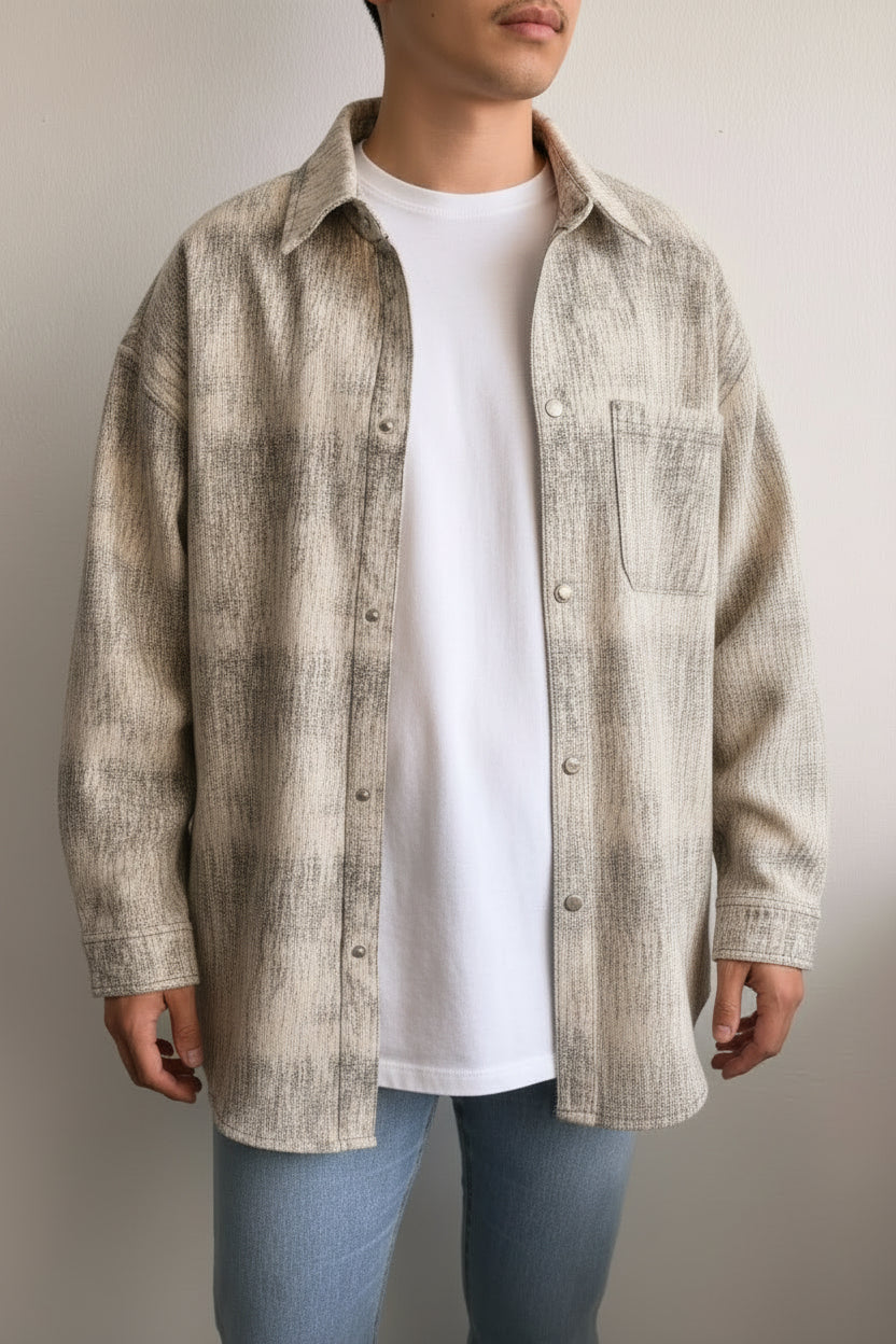 Person wearing a patterned shirt over a white t-shirt with light blue jeans on a neutral background
