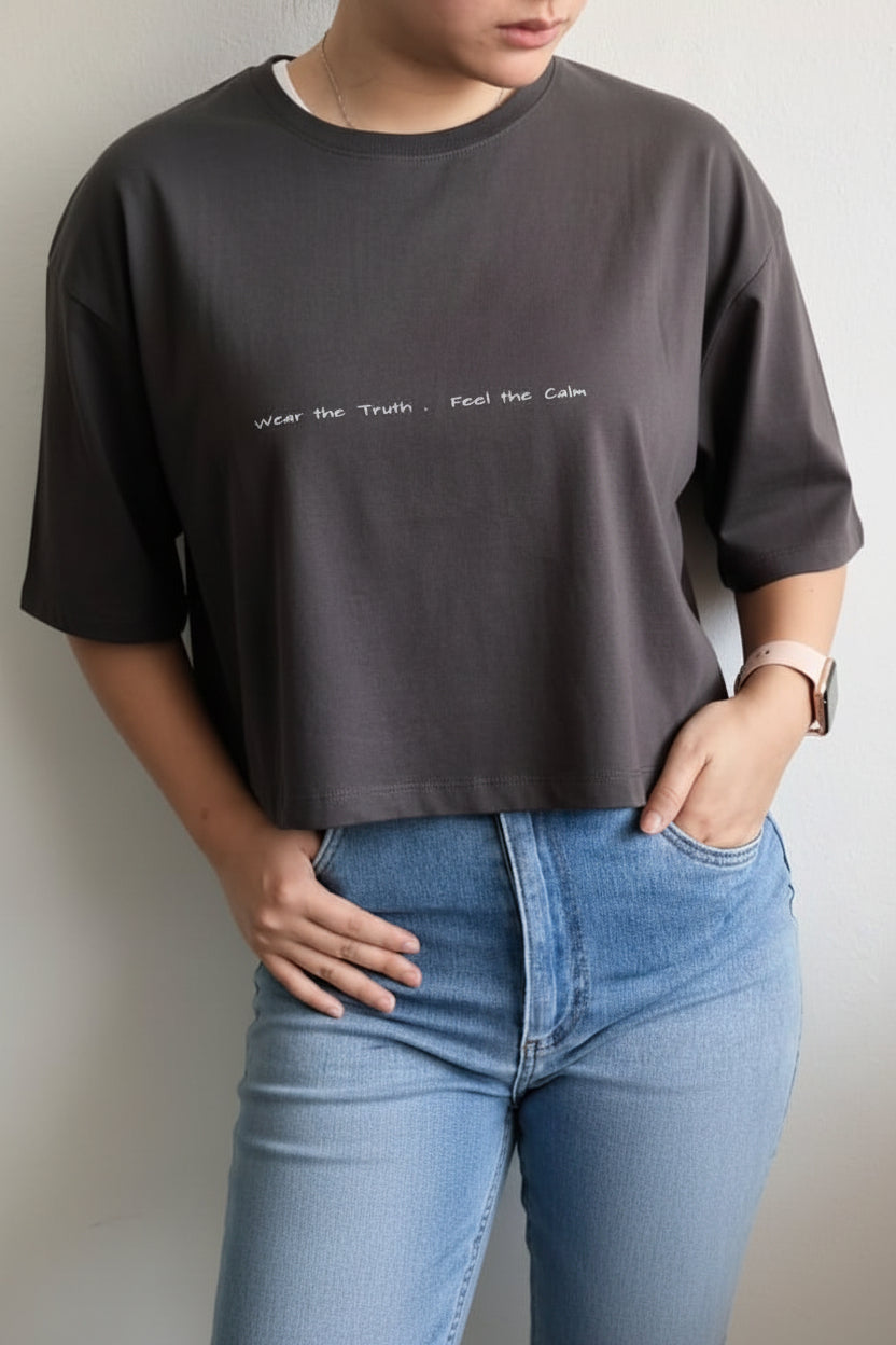 Person wearing a dark gray t-shirt with text and light blue jeans against a plain background