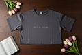 Gray t-shirt with text on a wooden surface with tulips and an open book.
