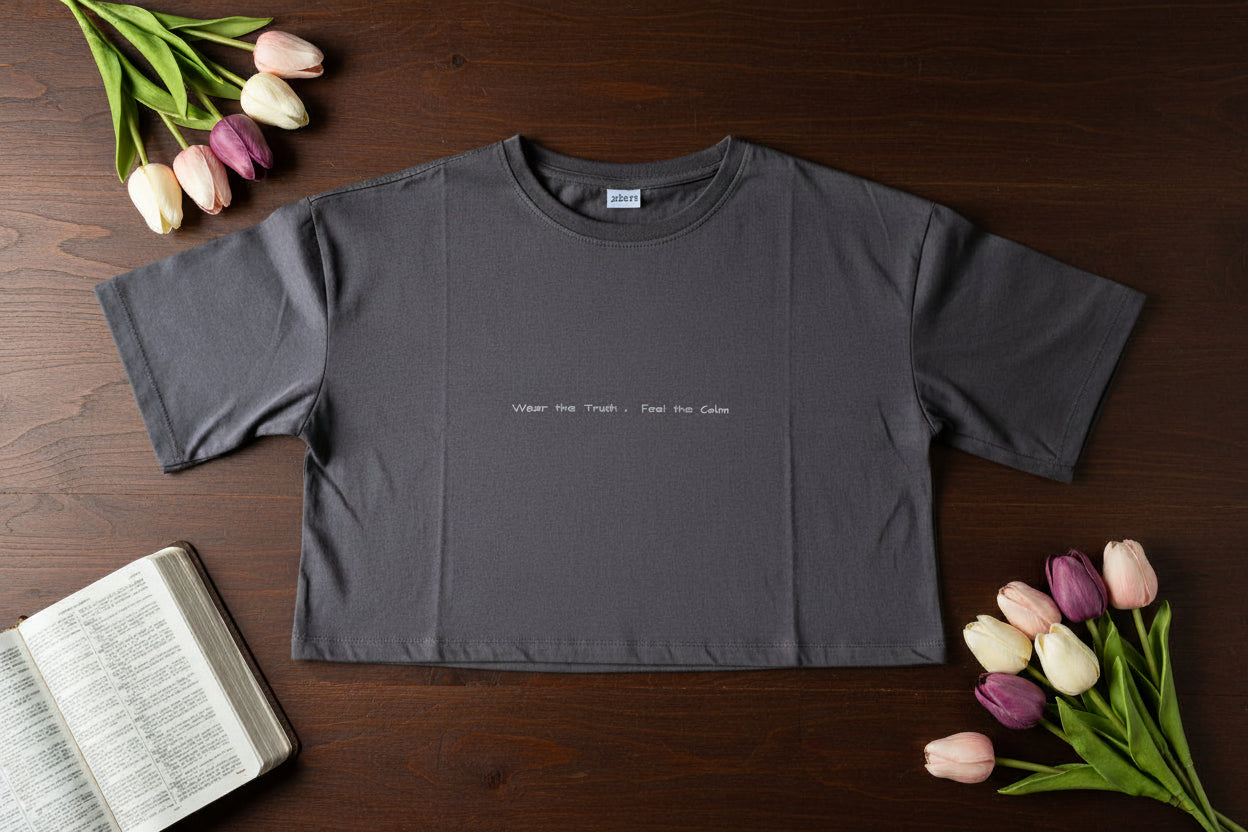 Gray t-shirt with text on a wooden surface with tulips and an open book.