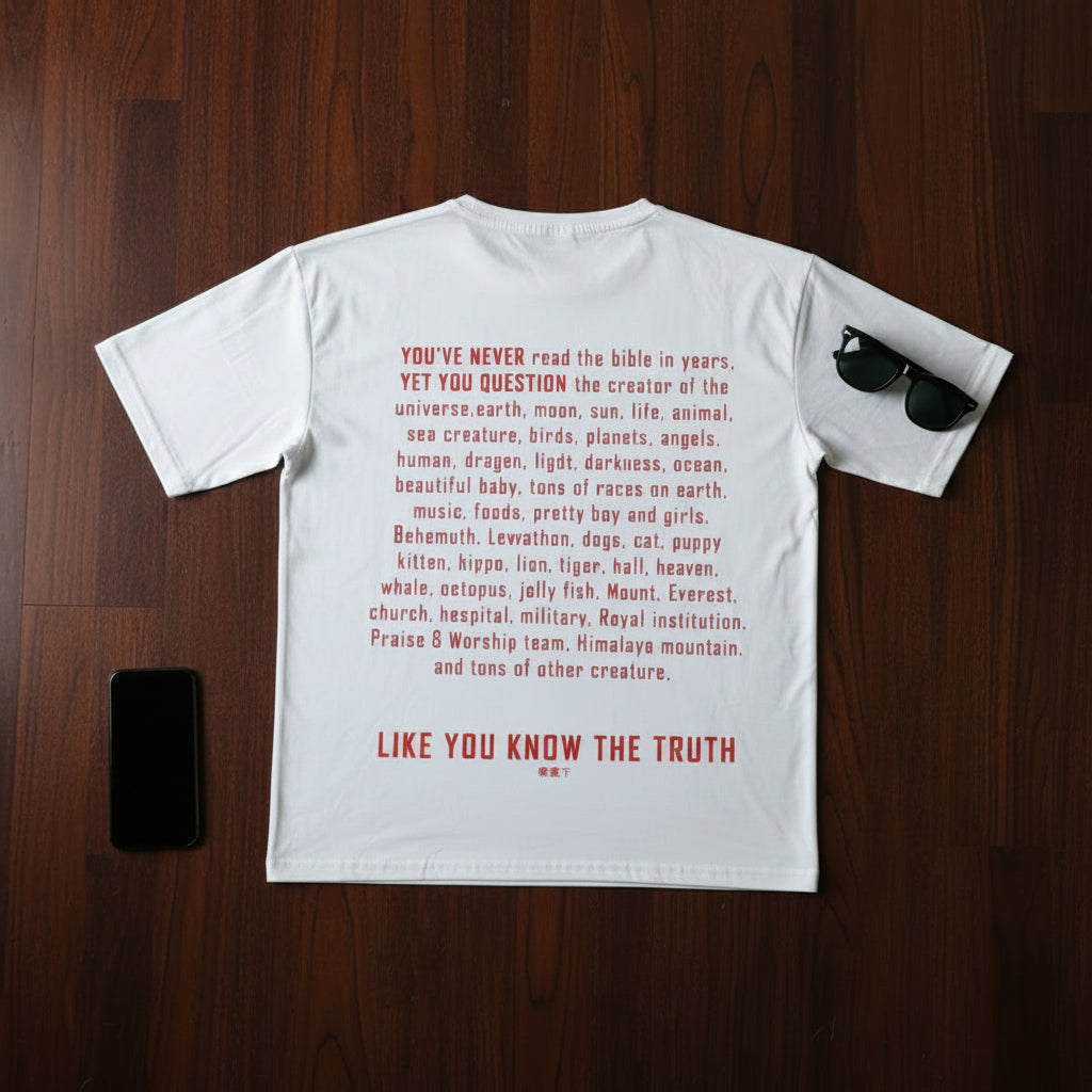 White t-shirt with red text on a wooden surface with sunglasses and phone.